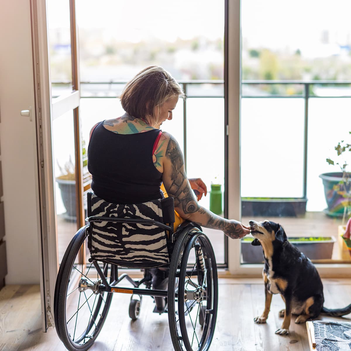 Wheelchair bound female looking out the window with her dog.